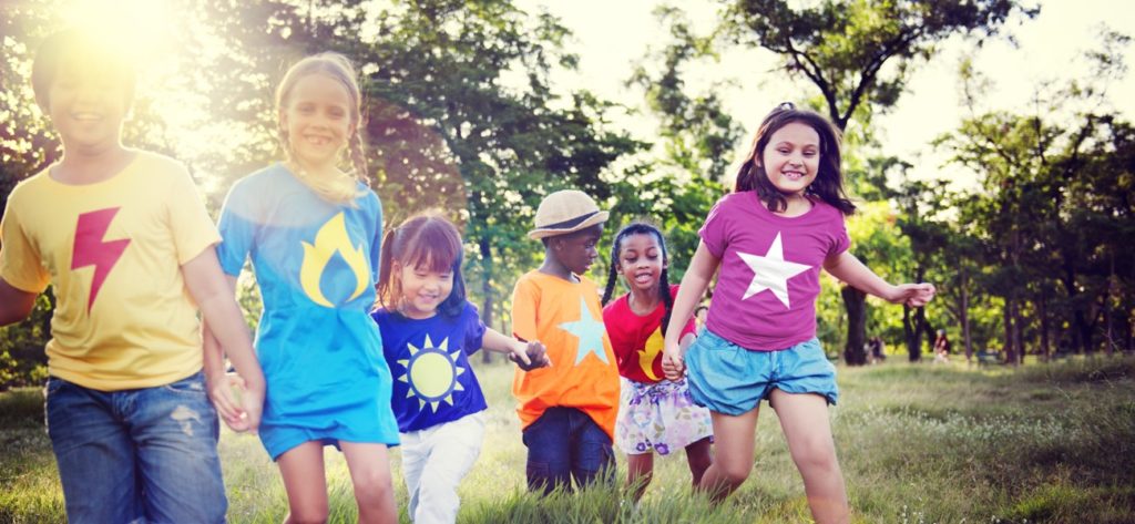 Kinder in bunten T-Shirts spielen auf einer grossen Wiese.