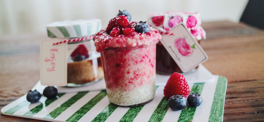 Einmachgläser mit Chiapudding und Beeren auf einem Anrichtebrettchen