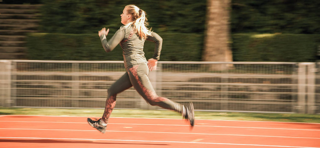 blonde Frau springt auf roter Finnenbahn mit grünem Sportoutfit